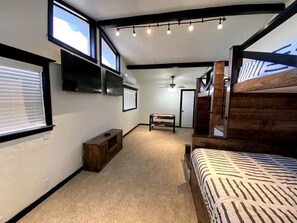 A bedroom with a bed, a bench, a TV, and a ceiling fan.