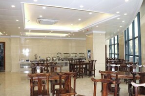 A spacious dining area with multiple wooden tables and chairs, a kitchen area in the background, and large windows allowing natural light. - Holiday Inn Bali (Rong County)