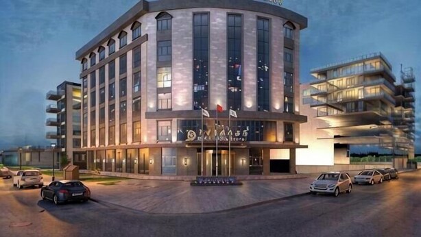 Un hôtel moderne à la façade incurvée, doté de plusieurs étages et d’une entrée imposante ornée de drapeaux.