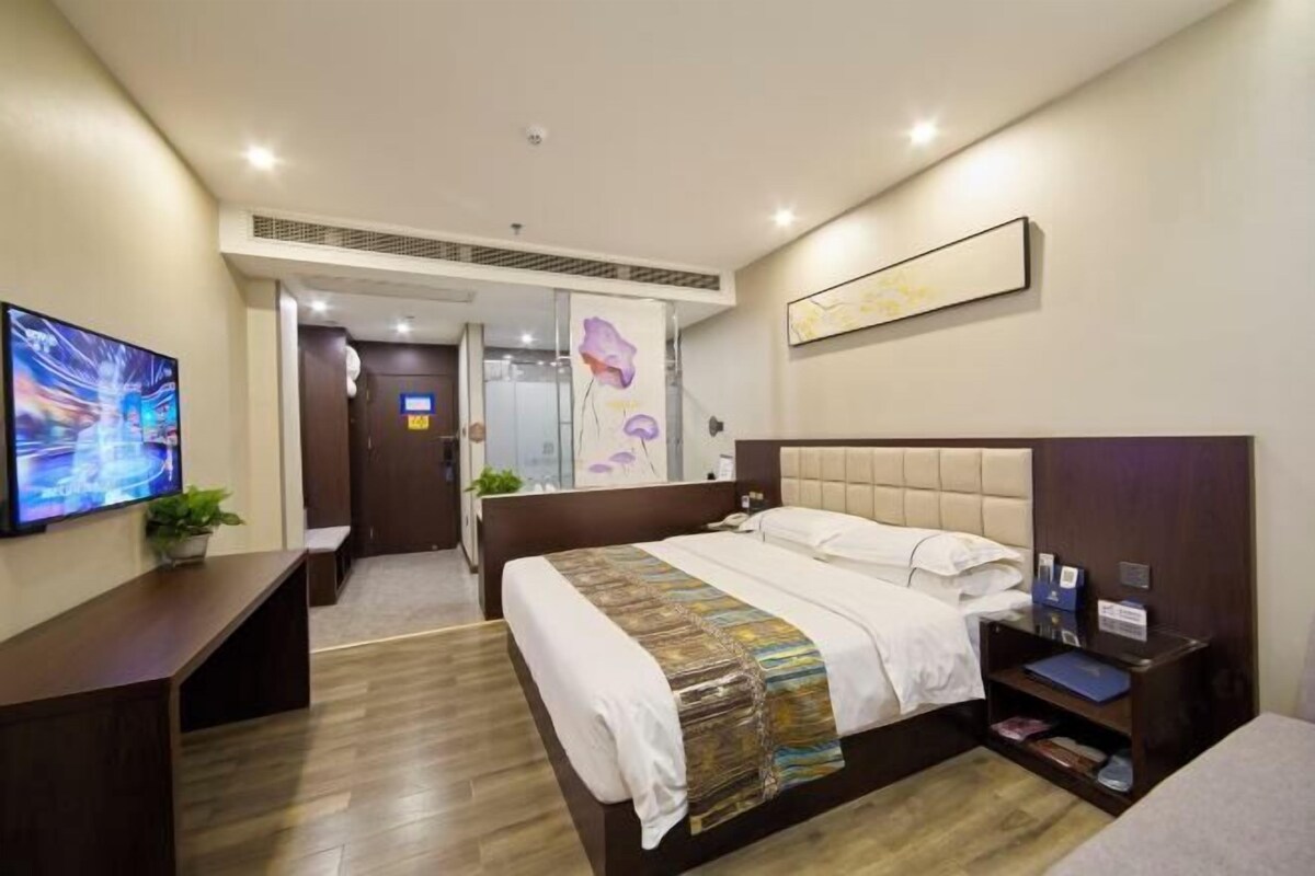 Une chambre d’hôtel avec un grand lit, un bureau, une télévision et une salle de bain visible à travers une porte en verre.