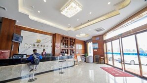 Un espace d’accueil d’hôtel doté d’un comptoir en marbre, d’étagères en bois et d’une grande fenêtre donnant sur le parking.