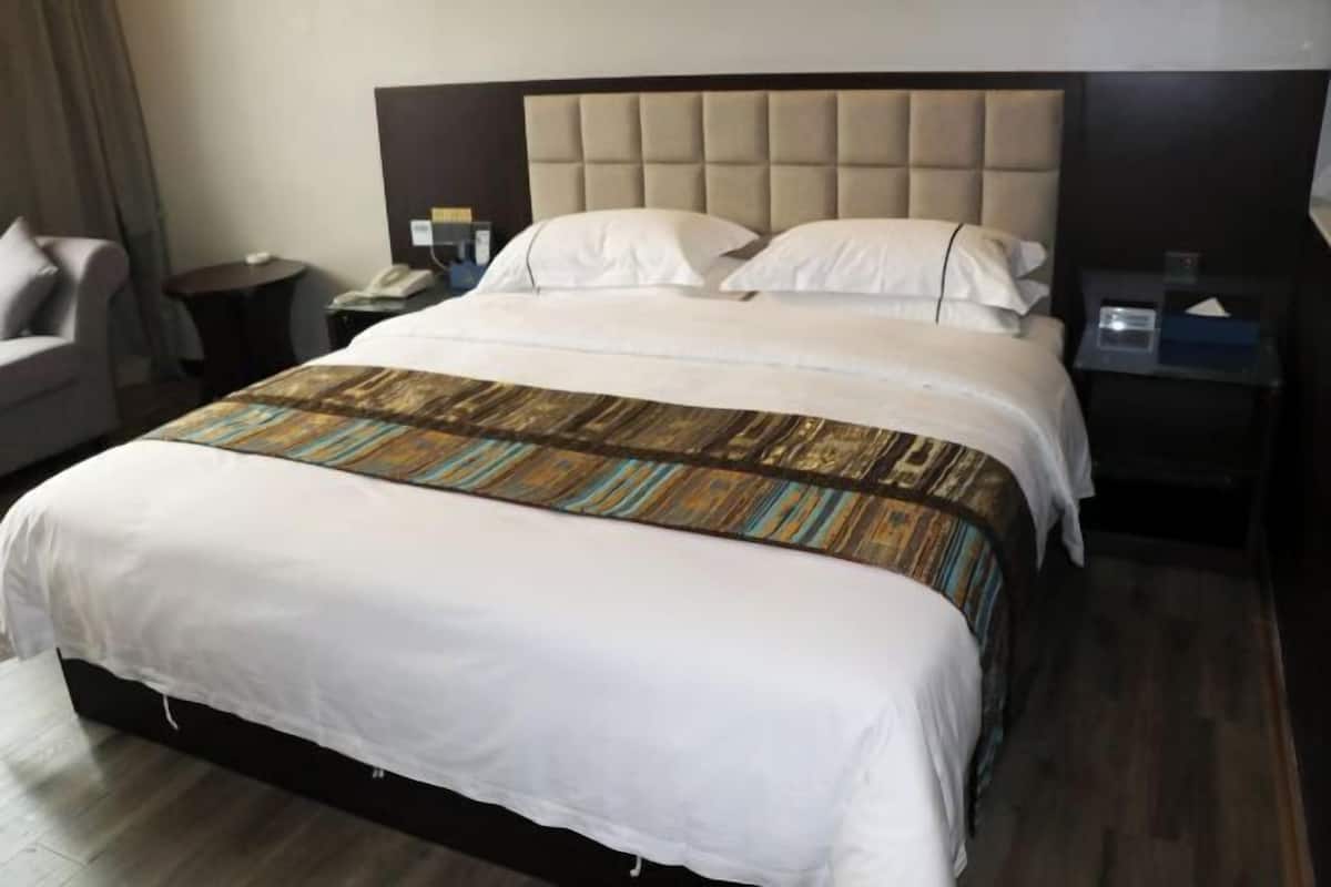 Camera d'albergo con un letto grande, una testata, un comodino con una lampada e una sedia.