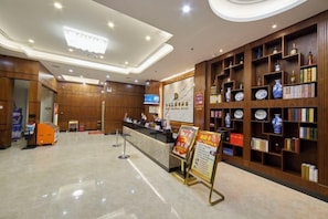 A hotel lobby with a reception desk, a digital screen, and a display board.