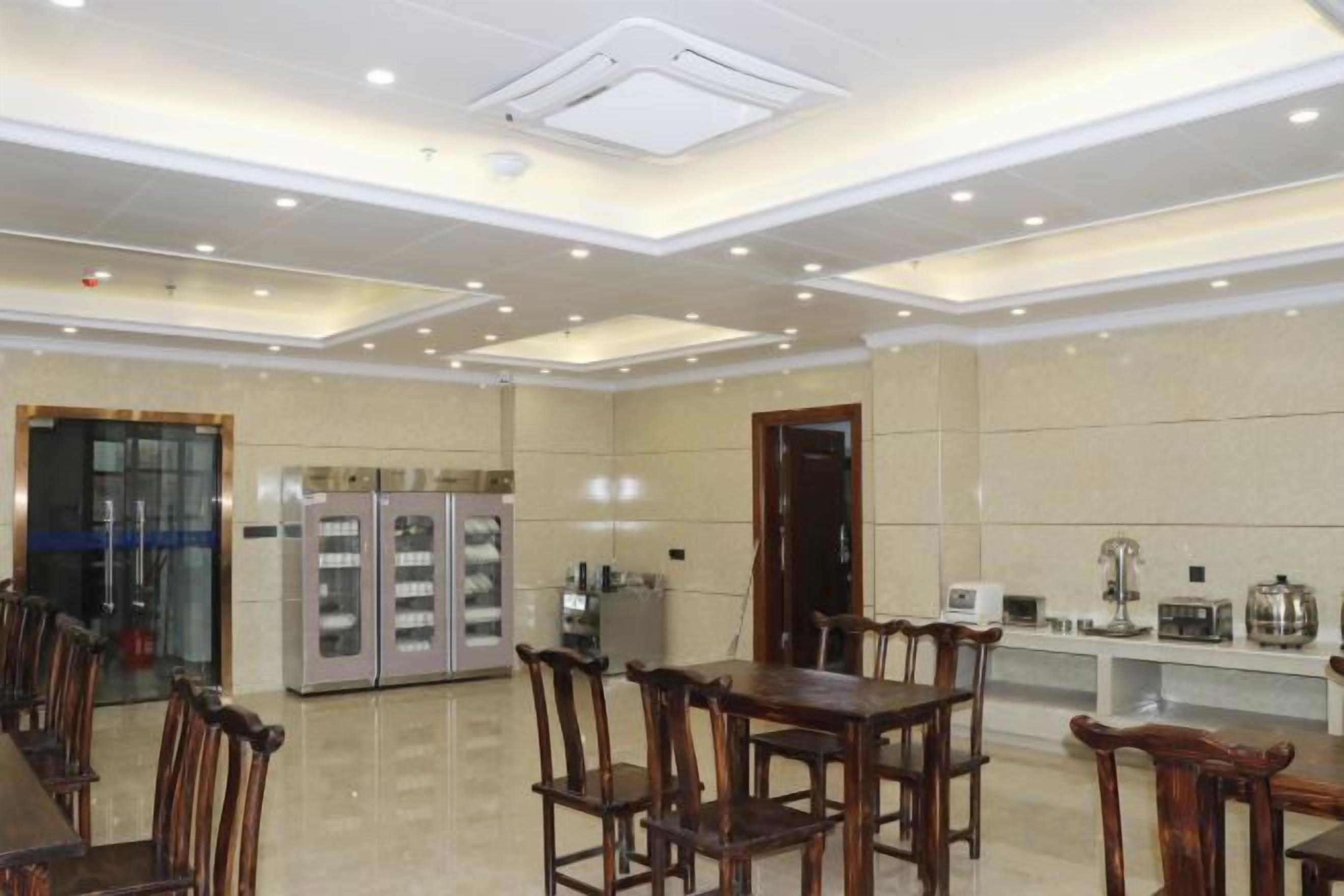Un comedor de hotel con una larga mesa de madera, sillas, un refrigerador y una estación de café.