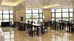Un vaste espace dédié à la salle à manger, avec de nombreuses tables et chaises, de grandes fenêtres laissant entrer la lumière naturelle et un plancher ciré.