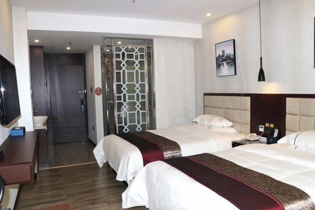 Camera d'albergo con due letti, una scrivania, una televisione e un bagno visibile tramite una porta in vetro.
