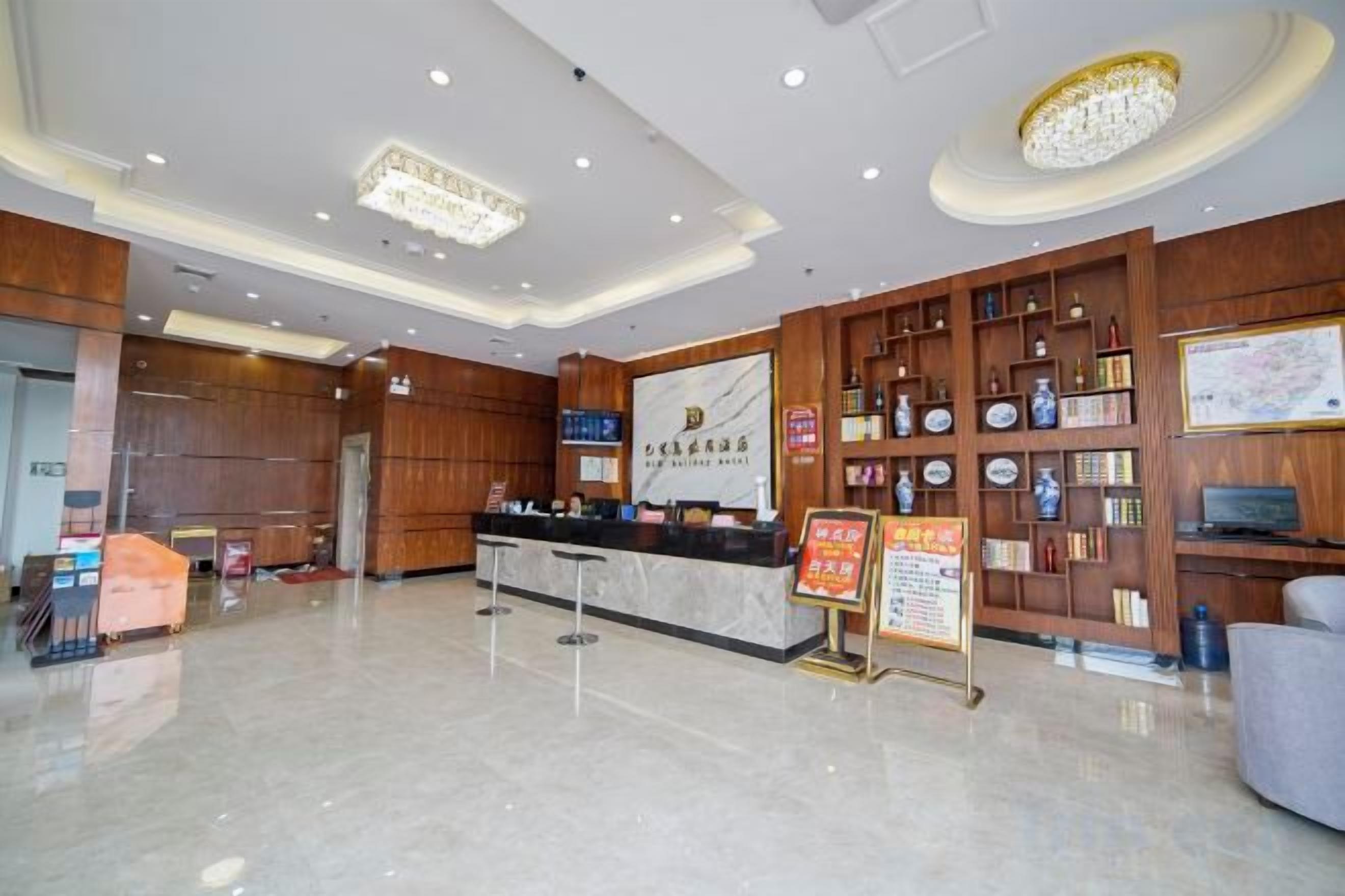 A hotel lobby with a reception desk, wooden paneling, a chandelier, and a wall with framed items.