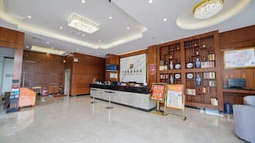 A hotel lobby with a reception desk, wooden paneling, a chandelier, and a wall with framed items.