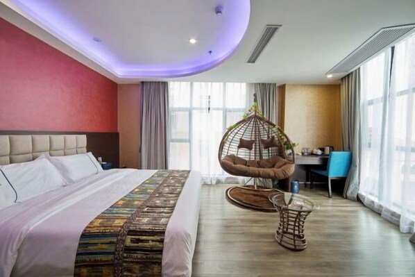 Une chambre d’hôtel avec un lit, un fauteuil suspendu, un bureau et de grandes fenêtres.