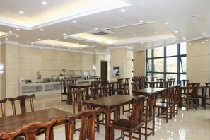 A spacious dining area with multiple wooden tables and chairs, a buffet line, and large windows providing natural light. - Holiday Inn Bali (Rong County)