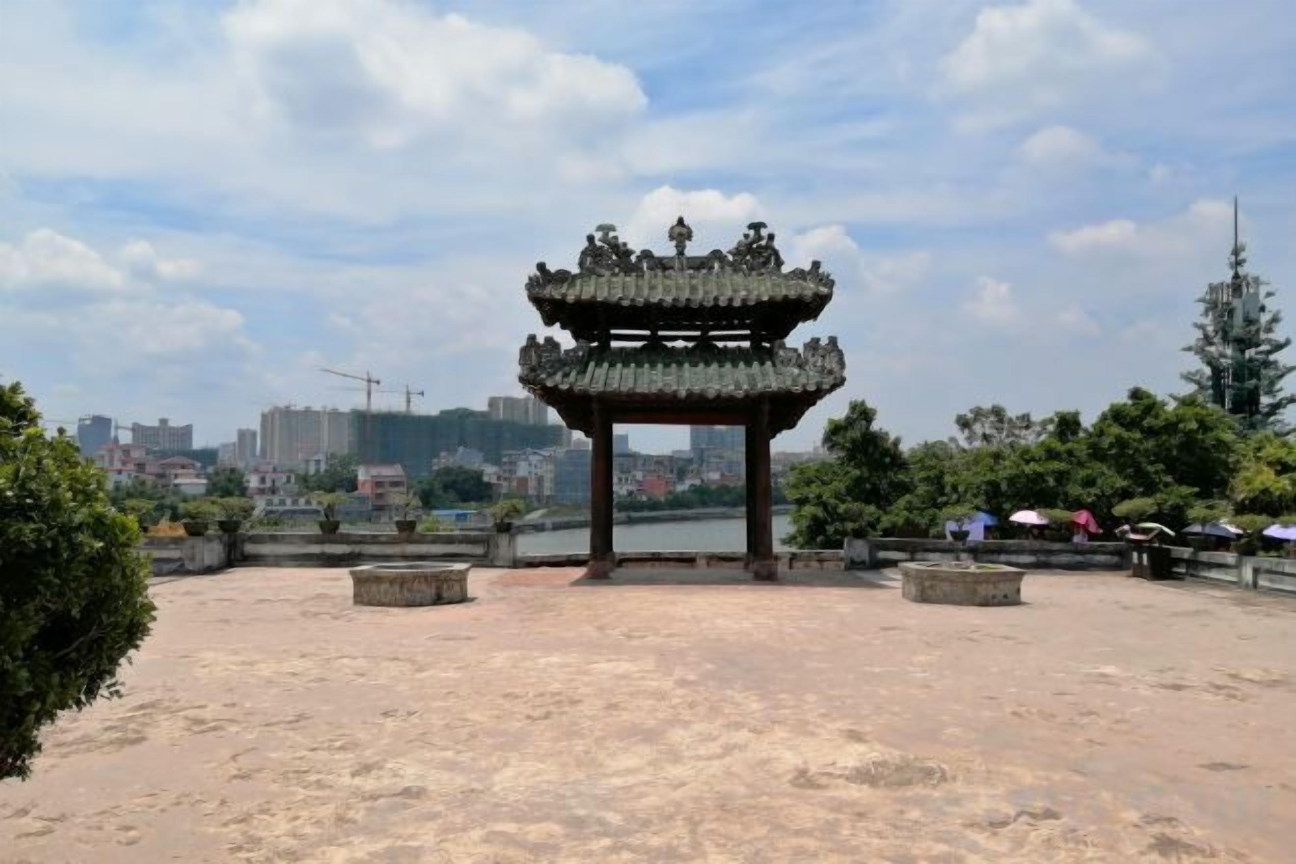 A traditional multi-tiered pavilion with a stone base, surrounded by a landscaped area with benches.