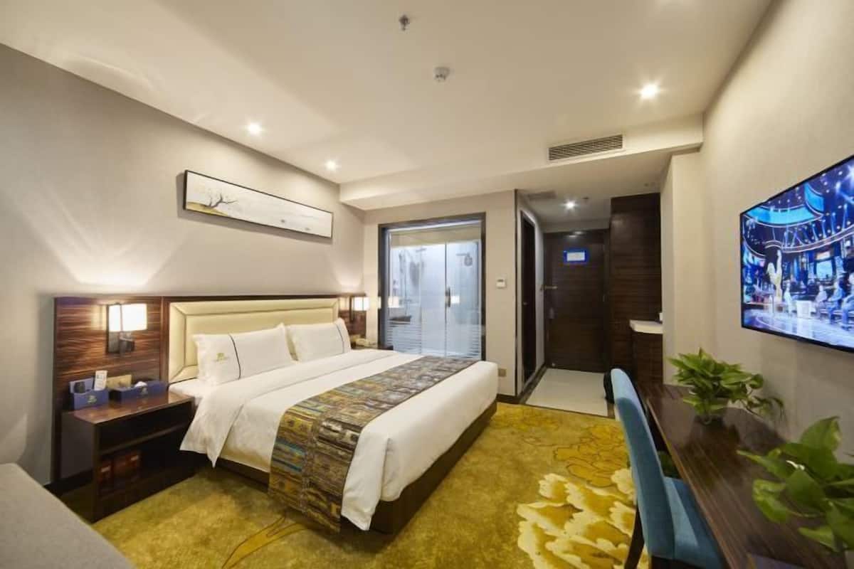 Camera d'albergo con un letto, comodino, televisore a parete e porta che conduce al bagno.