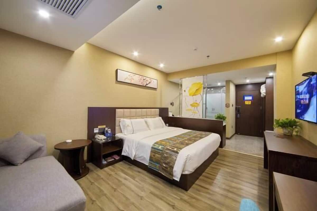 Una camera d'albergo con un letto, un divano, una televisione, un tavolino e uno specchio.