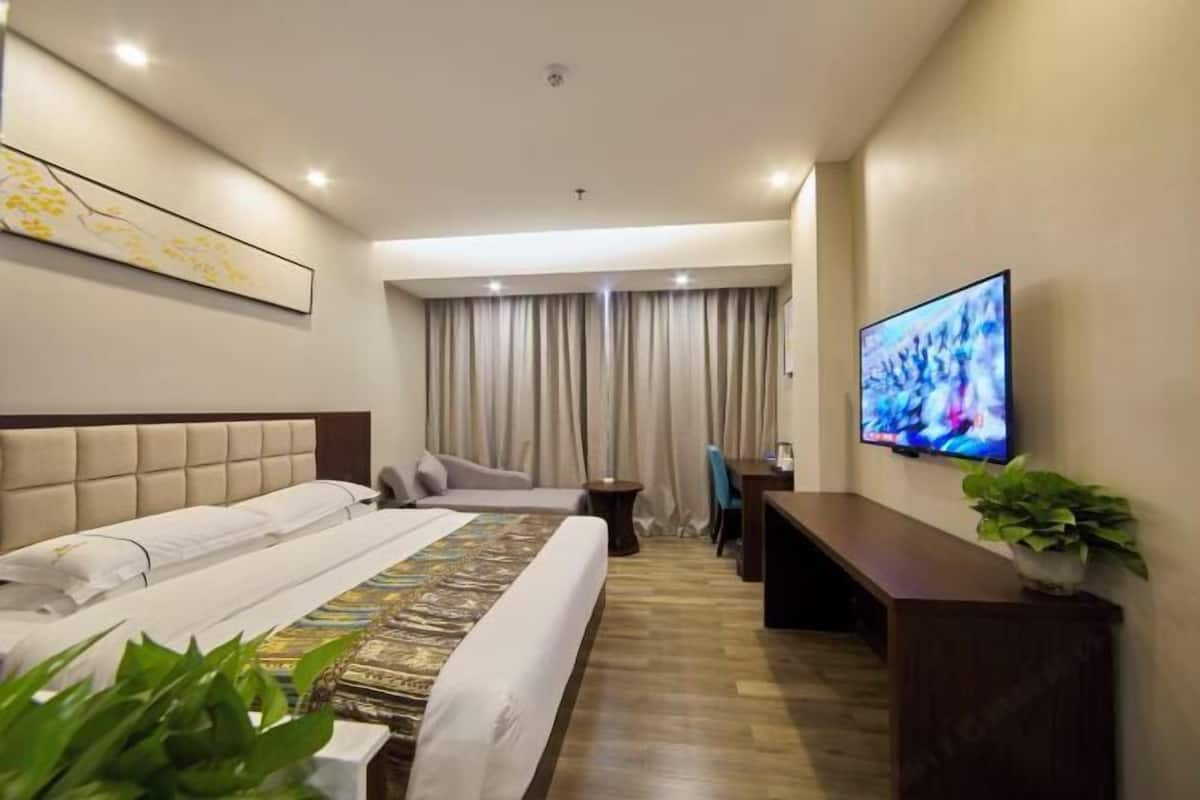 Una camera d'albergo con un letto, una scrivania, una TV e un'ampia finestra con tende.