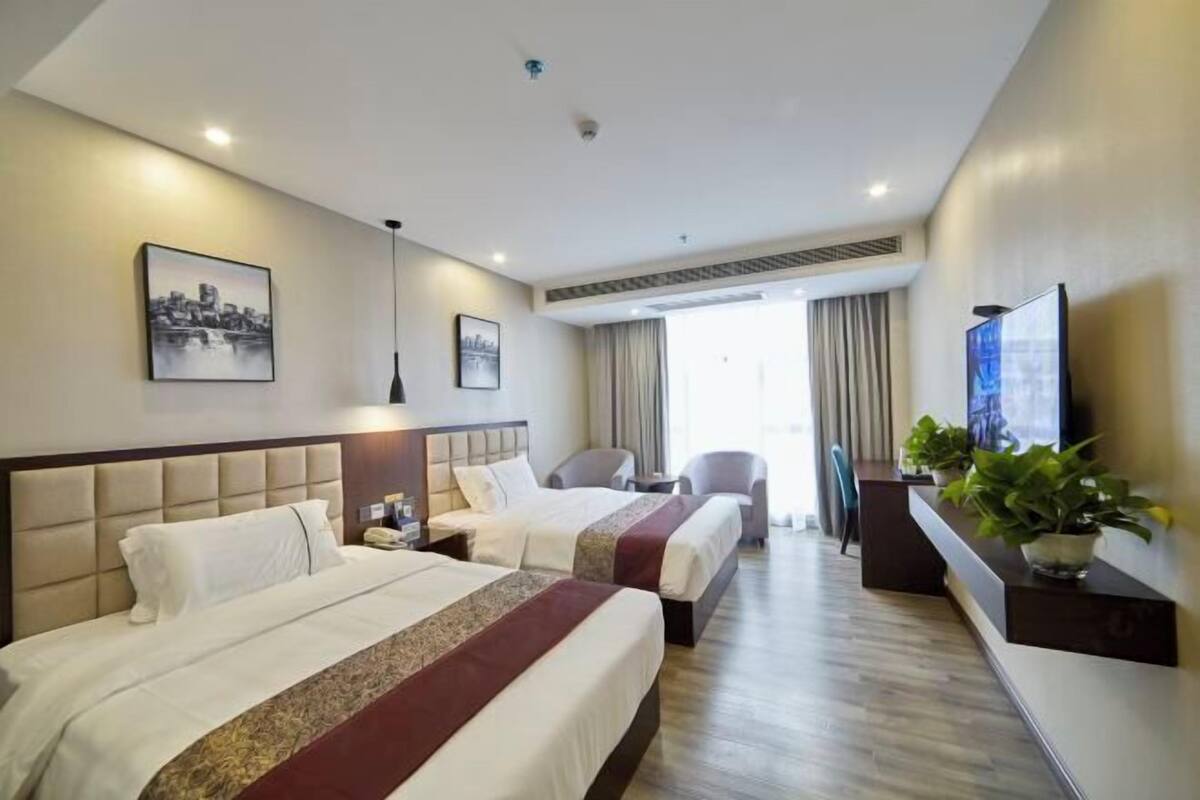 Una camera d'albergo con due letti, una televisione, una scrivania e una finestra con tende.