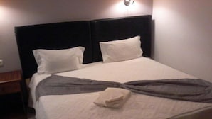 Un lit bien fait, avec une tête de lit sombre, des oreillers blancs et une serviette blanche pliée posée sur le lit.