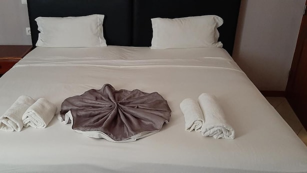 Un lit bien fait, avec du linge de lit blanc et marron, une table de chevet en bois et une tête de lit noire.
