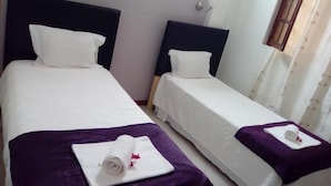 Deux lits simples avec des têtes de lit, du linge de lit blanc et des couvre-lits violets.