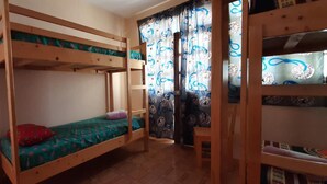 A bunk bed room with a wooden floor, a small table, and a curtain with a pattern.