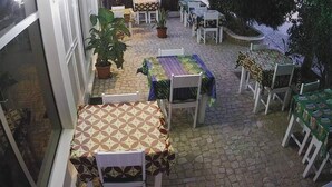Een terras buiten met tafels, stoelen, potplanten en een stenen vloer.