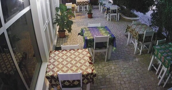 An outdoor patio area with tables and chairs, potted plants, and a stone floor. - Room-bed in Mixed Dormitory Room in Vila (Maio)