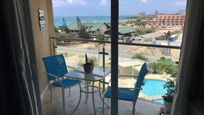 A balcony with a table and chairs, a potted plant, and a view of a beach and buildings. - Lovely Sea View,eagle Beach, Oasis Condominium Wifi (Oranjestad)