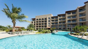 A hotel with a swimming pool, palm trees, and a multi-story building with balconies. - Lovely Sea View,eagle Beach, Oasis Condominium Wifi (Oranjestad)