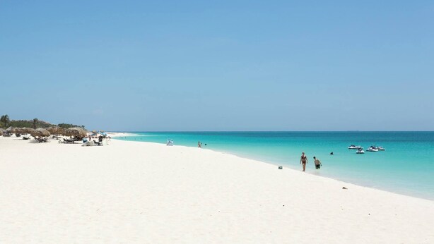 A beach with white sand, clear turquoise water, and a few people walking. - Lovely Sea View,eagle Beach, Oasis Condominium Wifi (Oranjestad)