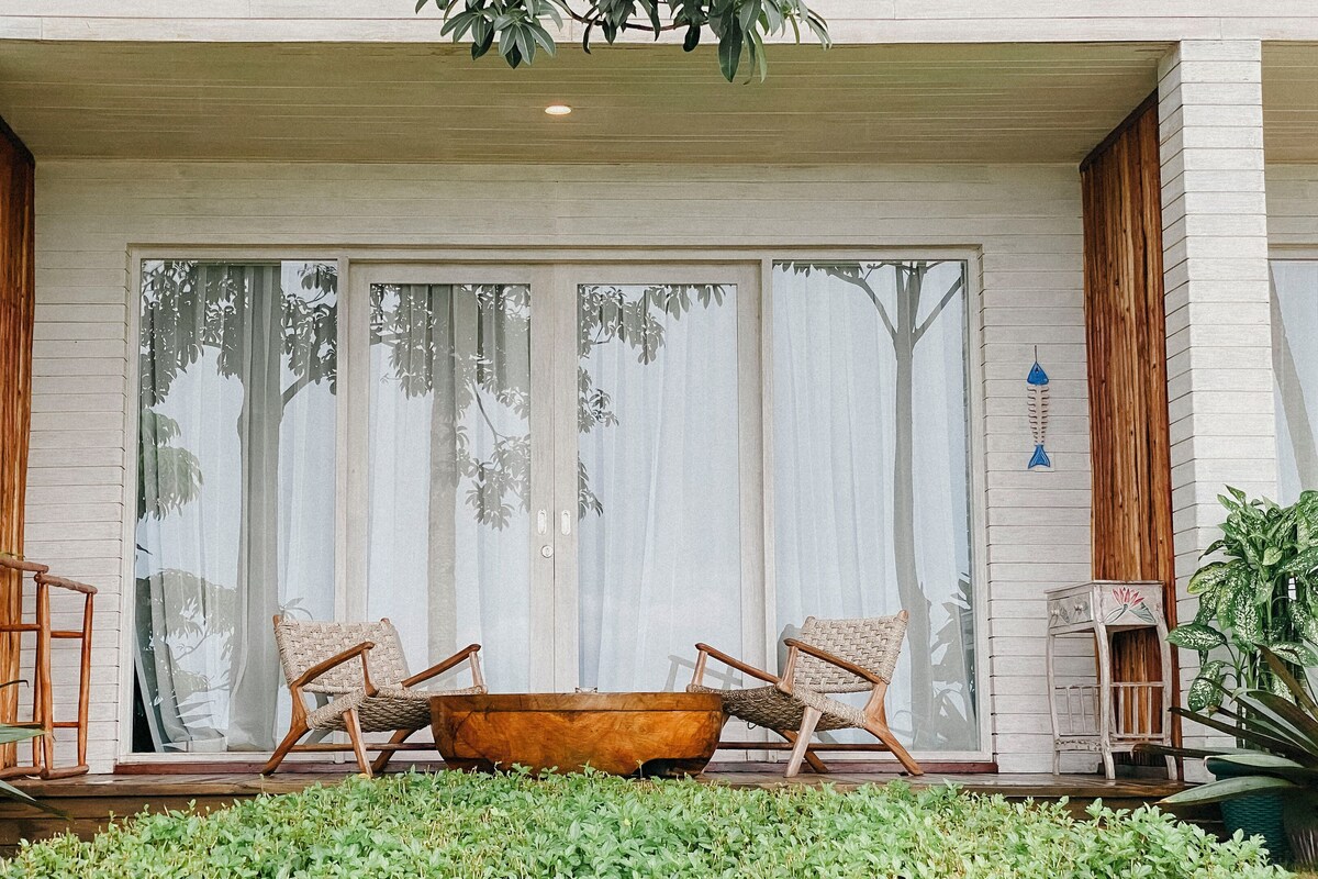 A modern house with a large sliding glass door, two wicker chairs, a wooden bathtub, and a small table.