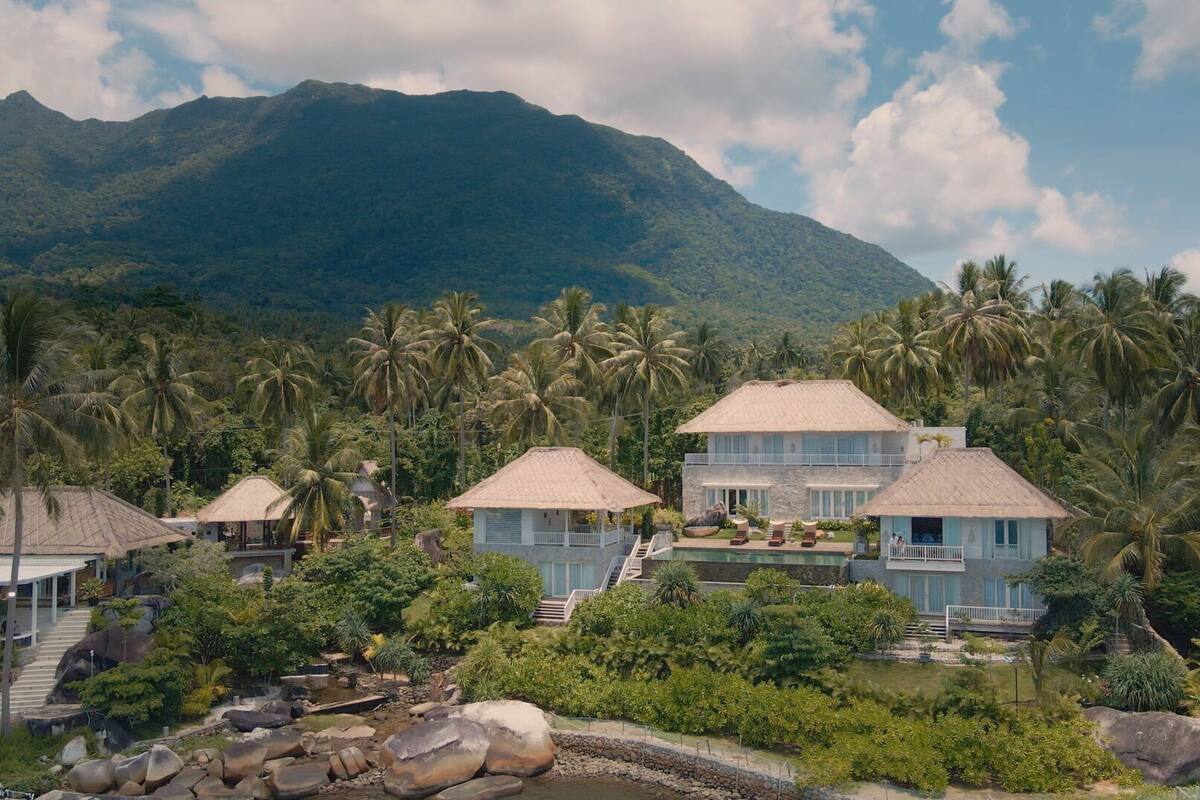 Un resort con varias edificaciones, una piscina y montañas al fondo.