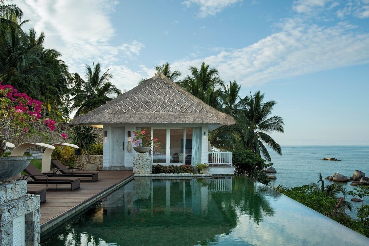 A resort with a pool, a thatched-roof structure, and palm trees.
