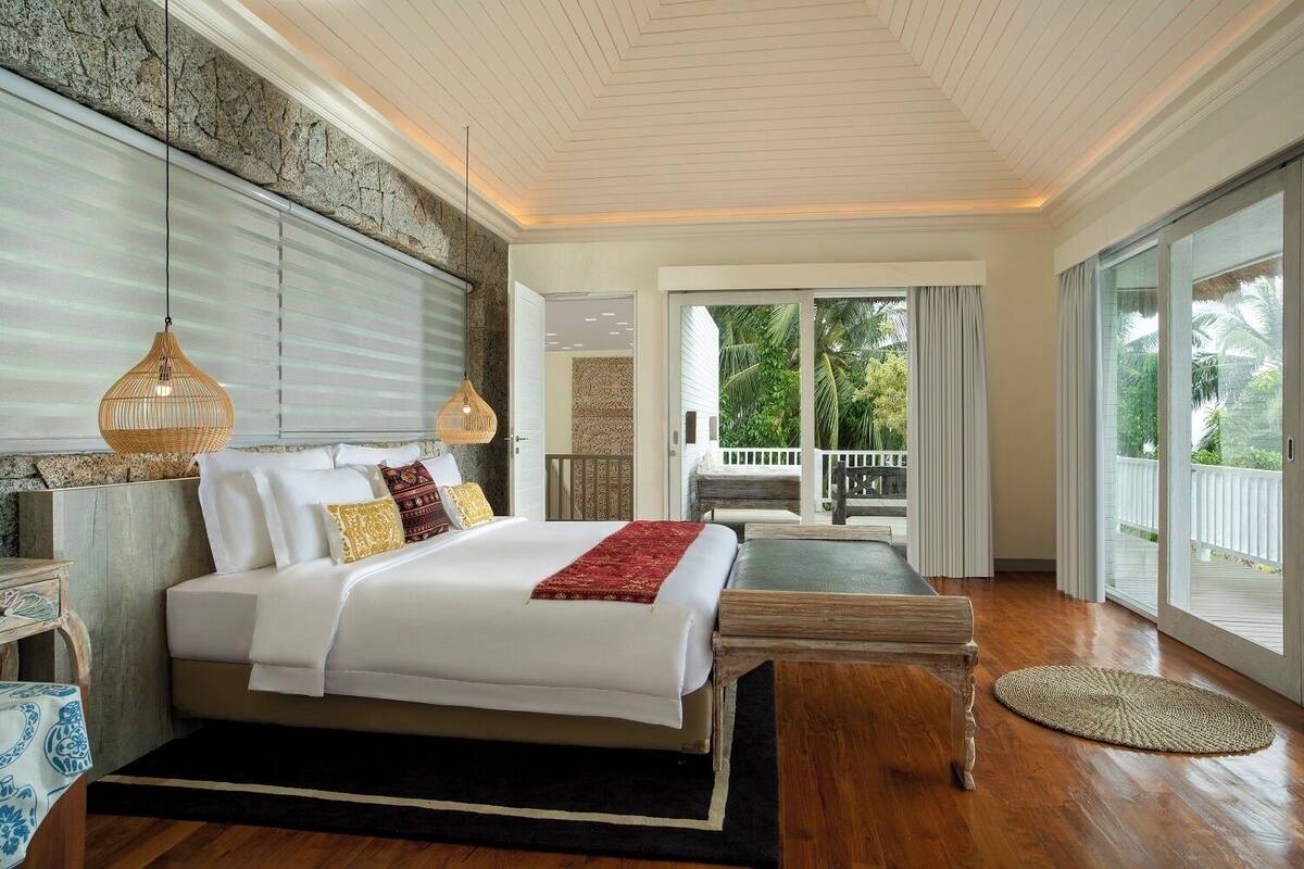 Un dormitorio amplio con una cama grande, un banco de madera y vistas al exterior a través de una puerta corredera.