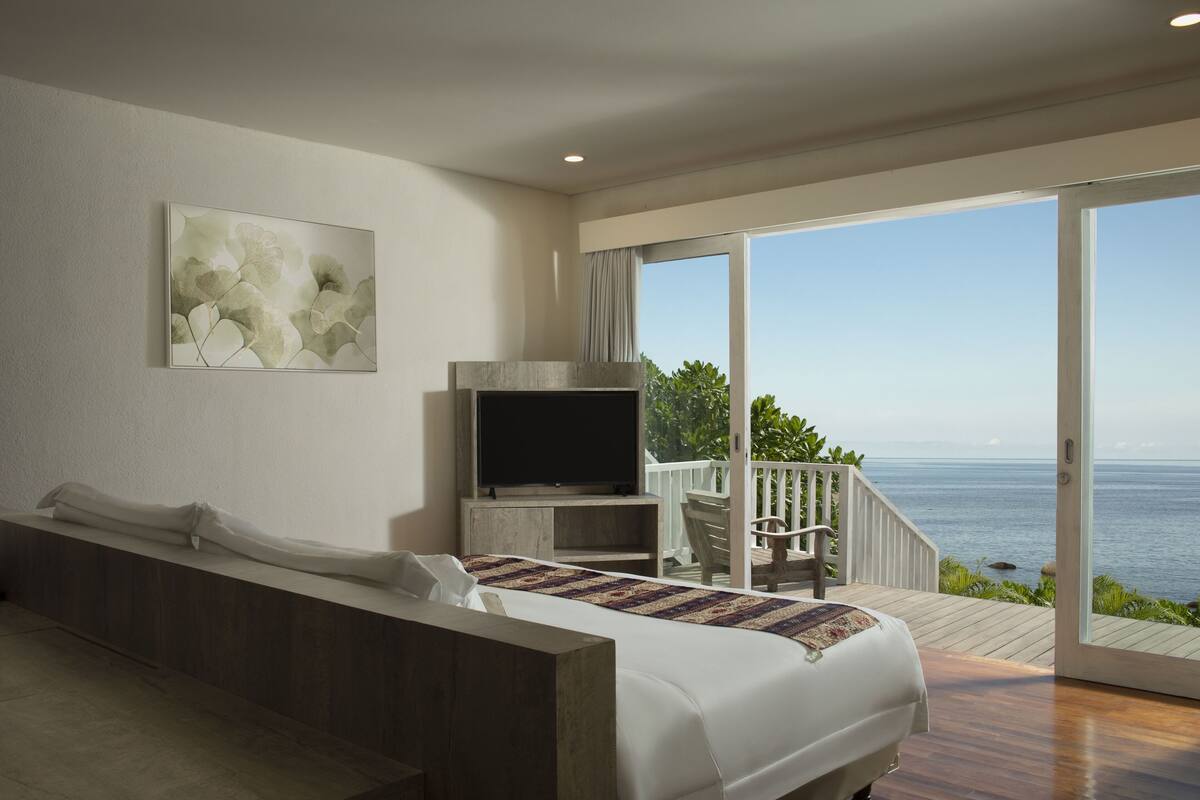 Un dormitorio con una cama grande, televisión y un balcón con vista al océano.