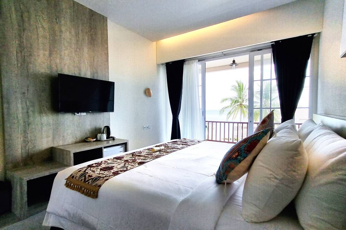Habitación de hotel con una cama, un televisor de pantalla plana montado en la pared, una mesita con una lámpara y una ventana con cortinas.