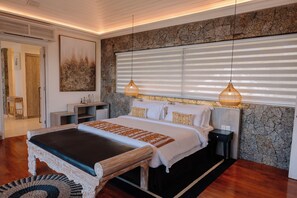 A bedroom with a large bed, a nightstand, a bedside table, a wall-mounted artwork, and a window with blinds. - Adiwana Jelita Sejuba Natuna (Sepempang)