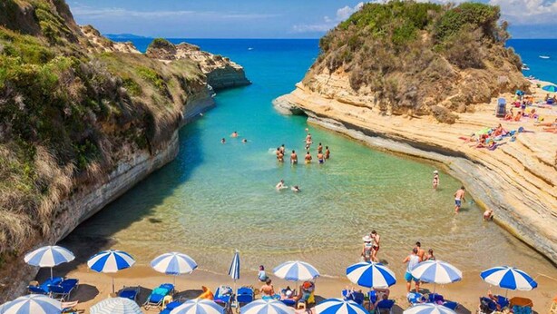 A coastal beach with clear waters, rocky cliffs, and beach umbrellas. - Summer Desire - Family Apartment With Sea View (Corfu)