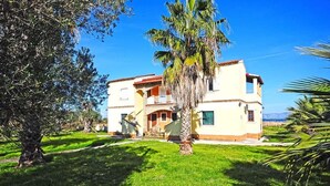 A two-story house with a balcony, surrounded by a well-maintained lawn and palm trees. - Summer Desire - One Bedroom Apartment With Sea View (Corfu)
