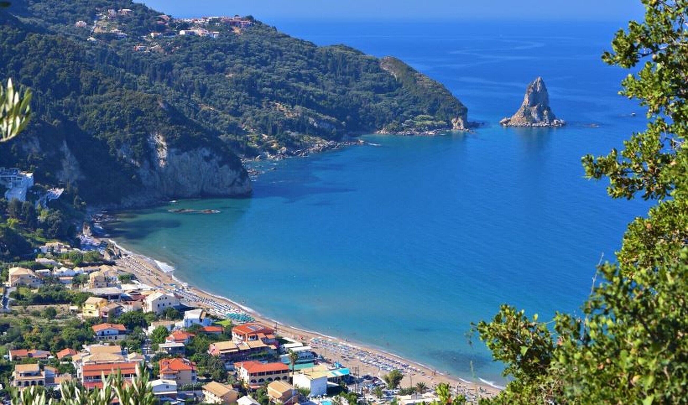 A coastal town with a beach, houses, and a rocky cliff.