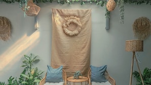 Une pièce décorée d’une grande tapisserie tissée, de fauteuils en osier avec des coussins et de plantes en pot.