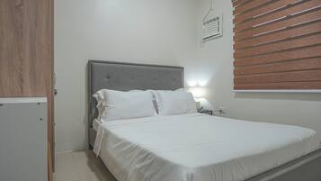 Een slaapkamer met een bed, een nachtkastje, een wandheater en een houten verstelbaar raambekleden.