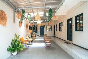 A corridor with chairs and tables, hanging plants, and a ceiling with a grid pattern. - Manzil Anilao Cosy 2 Bedroom Apartment U1 (Mabini)