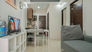 Una sala de estar con un sofá gris, un televisor, un comedor con sillas y una mesa, y una cocina al fondo.
