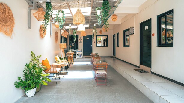 Un couloir agrémenté de chaises et de tables, de plantes suspendues et d’un plafond orné d’un motif en réseau.