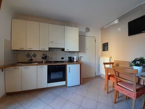 Une cuisine compacte avec des meubles blancs, une cuisinière, un petit réfrigérateur et un coin repas comprenant une table et des chaises en bois.