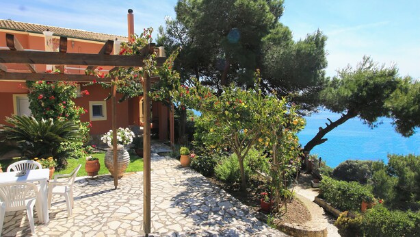 Un patio con pavimento in pietra, sedie bianche, un tavolo e vasi con piante.