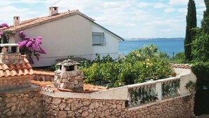 Une maison située sur la côte, dotée d’un mur en pierre, d’un toit en tuiles et offrant une vue sur la mer.