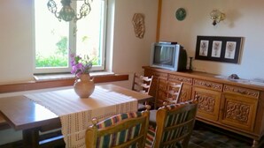 Un coin repas comprenant une table, des chaises, un vase avec des fleurs, un téléviseur et un meuble.
