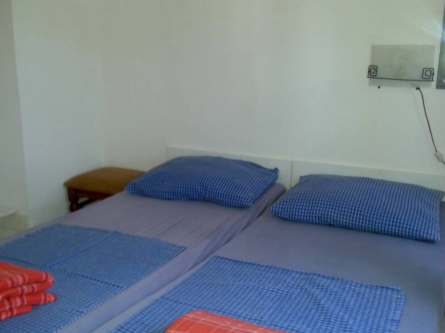 Une chambre simple avec deux lits, chacun agrémenté d’oreillers à carreaux bleus et de draps gris.