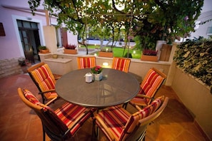 A round outdoor dining table with six striped chairs, surrounded by potted plants and a view of a garden. - Spacious Apartment Milly With Pool (Preko)