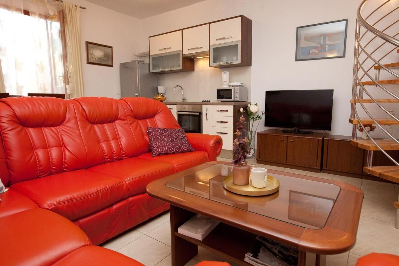 A modern living room with a red leather sofa, a wooden coffee table, a flat-screen TV, and a kitchen area with cabinets and a microwave.